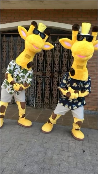 Duas girafas amarelas de óculos escuros e camisa estampada dançando na calçada