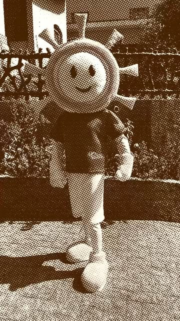 Mascote Lumi, um sol sorridente de corpo inteiro, em foto com filtro sépia